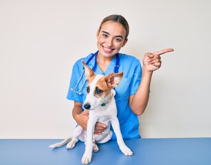 Young beautiful blonde veterinarian woman checking dog health smiling happy pointing with hand and...