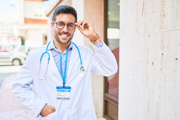 Young handsome hispanic doctor wearing uniform and stethoscope smiling happy. Standing with smile on face at town street.