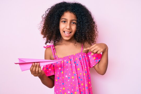 African american child with curly hair holding paper airplane pointing finger to one self smiling happy and proud