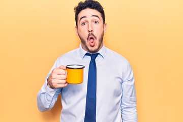 Young hispanic man wearing business clothes holding coffee scared and amazed with open mouth for surprise, disbelief face