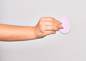 Hand of caucasian young woman holding pink makeup sponge over isolated white background