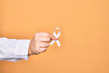 Hand of caucasian young woman holding white ribbon over isolated yellow background
