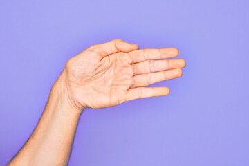 Hand of caucasian young man showing fingers over isolated purple background stretching and reaching with open hand for handshake, showing palm