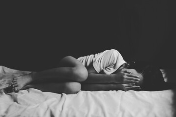 Sad little girl covers face with both hands lying in bed room. black and white image
