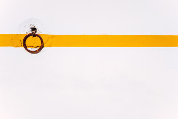 Rural background of a rusty ring on a white wall with orange line to tie animals.