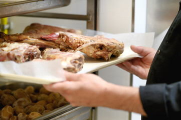 Unrecognizable chef putting baking tray with meat into rack in commercial kitchen. High quality photo