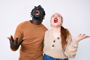 Interracial couple wearing casual clothes crazy and mad shouting and yelling with aggressive expression and arms raised. frustration concept.