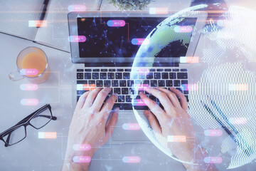 Multi exposure of man's hands typing over computer keyboard and world map hologram drawing. Top view. Technology concept.