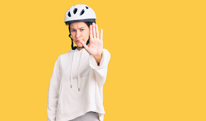 Beautiful brunette young woman wearing bike helmet and sporty clothes doing stop sing with palm of the hand. warning expression with negative and serious gesture on the face.