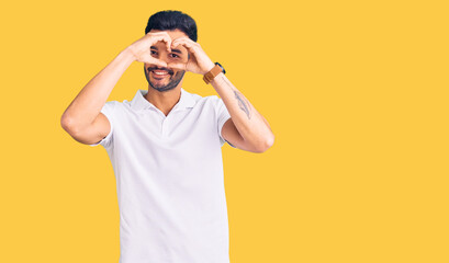 Young handsome hispanic man wearing casual clothes doing heart shape with hand and fingers smiling looking through sign