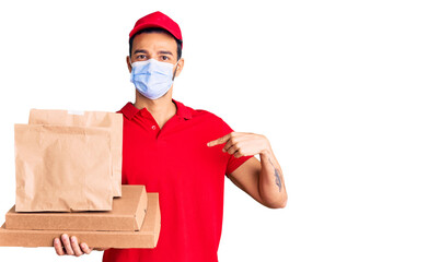 Fototapeta na wymiar Young handsome hispanic man delivering food wearing covid-19 safety mask pointing finger to one self smiling happy and proud