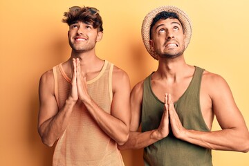 Young gay couple wearing summer clothes begging and praying with hands together with hope expression on face very emotional and worried. begging.