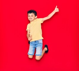 Adorable kid wearing casual clothes jumping over isolated red background