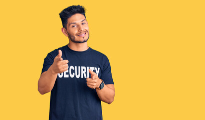 Handsome latin american young man wearing security t shirt pointing fingers to camera with happy and funny face. good energy and vibes.