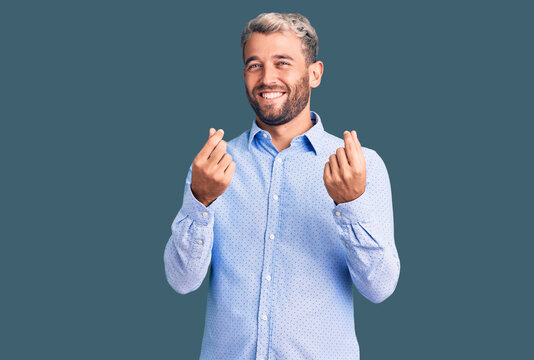 Young handsome blond man wearing elegant shirt doing money gesture with hands, asking for salary payment, millionaire business