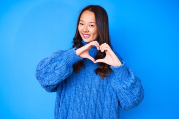 Young beautiful chinese girl wearing casual winter sweater smiling in love doing heart symbol shape with hands. romantic concept.