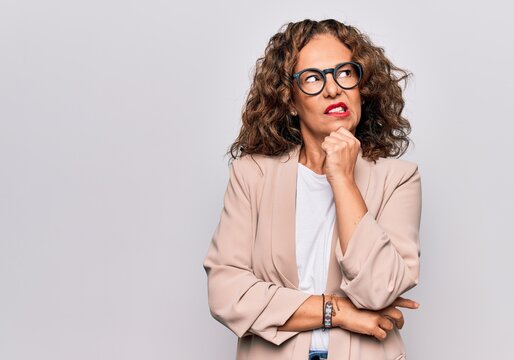 Middle age beautiful businesswoman wearing glasses standing over isolated white background thinking concentrated about doubt with finger on chin and looking up wondering