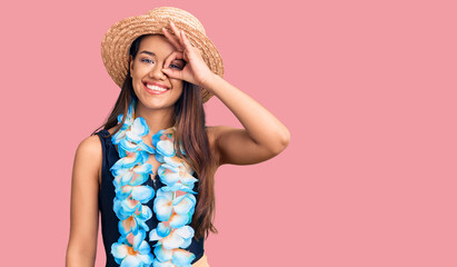 Young beautiful latin girl wearing hawaiian lei and summer hat doing ok gesture with hand smiling,...