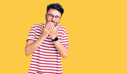 Young hispanic man wearing casual clothes laughing and embarrassed giggle covering mouth with...
