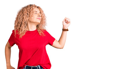 Young blonde woman with curly hair wearing casual red tshirt stretching back, tired and relaxed,...