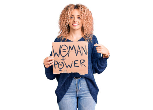 Young blonde woman with curly hair holding we need a change banner smiling happy pointing with hand and finger