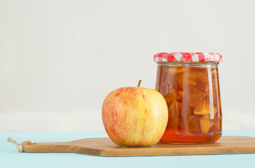 Glass jar of homemade apple jam with checkered lid and apple