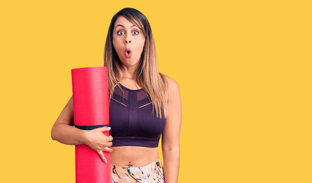 Young beautiful woman wearing sportswear holding yoga mat scared and amazed with open mouth for surprise, disbelief face
