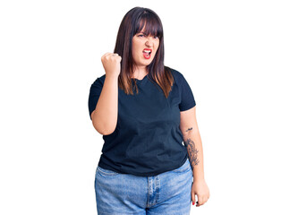 Young plus size woman wearing casual clothes angry and mad raising fist frustrated and furious while shouting with anger. rage and aggressive concept.
