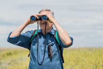 Man looking through binoculars searching for wildlife on a hike in a beautiful meadow background