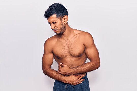Young latin man standing shirtless with hand on stomach because nausea, painful disease feeling unwell. ache concept.