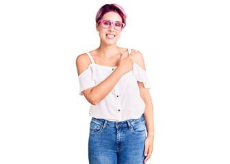 Young beautiful woman with pink hair wearing casual clothes and glasses cheerful with a smile of face pointing with hand and finger up to the side with happy and natural expression on face