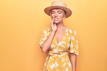 Beautiful blonde woman on vacation wearing summer hat and dress over yellow background touching mouth with hand with painful expression because of toothache or dental illness on teeth. Dentist
