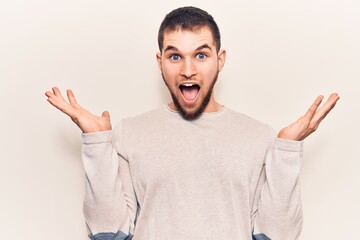 Young handsome man wearing casual sweater celebrating victory with happy smile and winner expression with raised hands