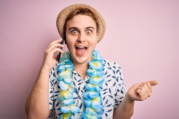 Young man on vacation wearing hat and hawaiian lei having conversation talking on smartphone...