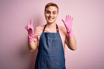Young handsome redhead cleaner man doing housework wearing apron and gloves showing and pointing up with fingers number six while smiling confident and happy.