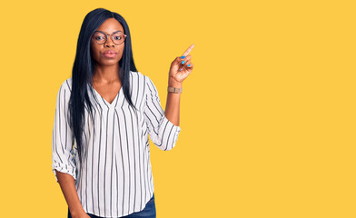 Young african american woman wearing casual clothes and glasses pointing with hand finger to the side showing advertisement, serious and calm face