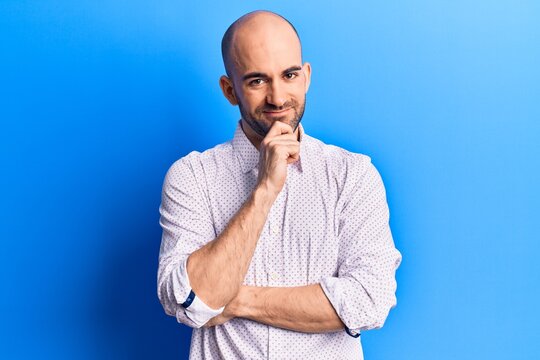 Young handsome bald man wearing elegant shirt smiling looking confident at the camera with crossed arms and hand on chin. thinking positive.