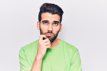Young handsome man with beard wearing casual t-shirt serious face thinking about question with hand on chin, thoughtful about confusing idea