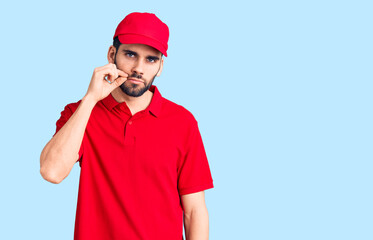 Young handsome man with beard wearing delivery uniform mouth and lips shut as zip with fingers....