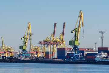 Fototapeta premium Sea commercial port. Loading and unloading operations in the port. Cranes and cargo containers on the shore. Merchant fleet. Shipping.