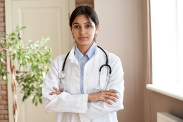 Confident young adult indian female doctor gp wear white coat stethoscope looking at camera...