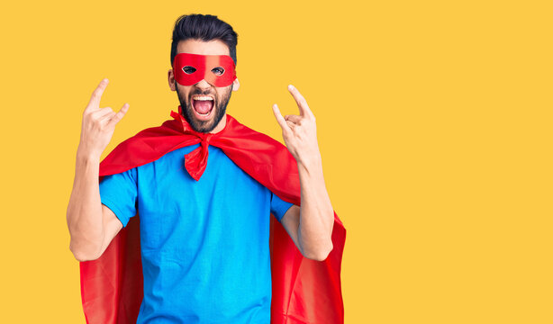 Young handsome man with beard wearing super hero costume shouting with crazy expression doing rock symbol with hands up. music star. heavy concept.