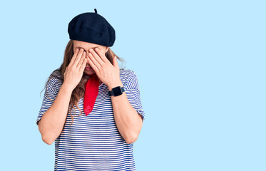 Young beautiful blonde woman wearing french beret and striped t-shirt rubbing eyes for fatigue and...