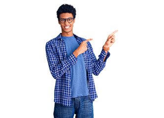 Young african american man wearing casual clothes and glasses smiling and looking at the camera pointing with two hands and fingers to the side.