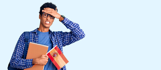 Young african american man wearing student backpack holding spanish flag stressed and frustrated with hand on head, surprised and angry face