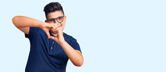 Naklejka premium Little boy kid wearing casual clothes and glasses smiling in love doing heart symbol shape with hands. romantic concept.