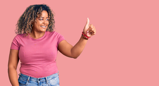 Young african american plus size woman wearing casual clothes looking proud, smiling doing thumbs up gesture to the side