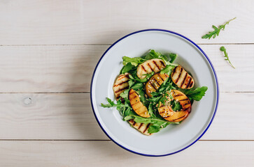 Grilled Halloumi Cheese salad with peach and arugula on a white wooden background. Healthy food concept.