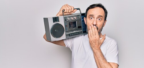 Middle age handsome man listening vintage boombox over isolated white background covering mouth with hand, shocked and afraid for mistake. Surprised expression
