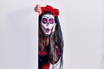 Young woman wearing day of the dead custome holding blank empty banner afraid and shocked, surprise and amazed expression with hands on face